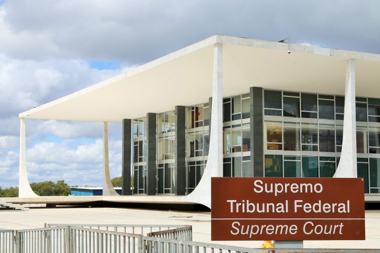 Prédio branco com fachada de vidro e uma placa marrom onde se lê: Supremo Tribunal Federal
