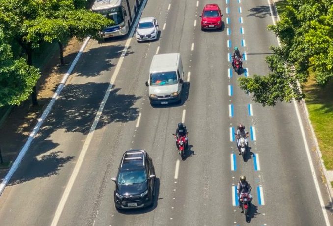 Motos trafegam numa faixa azul pintada numa avenida de São Paulo