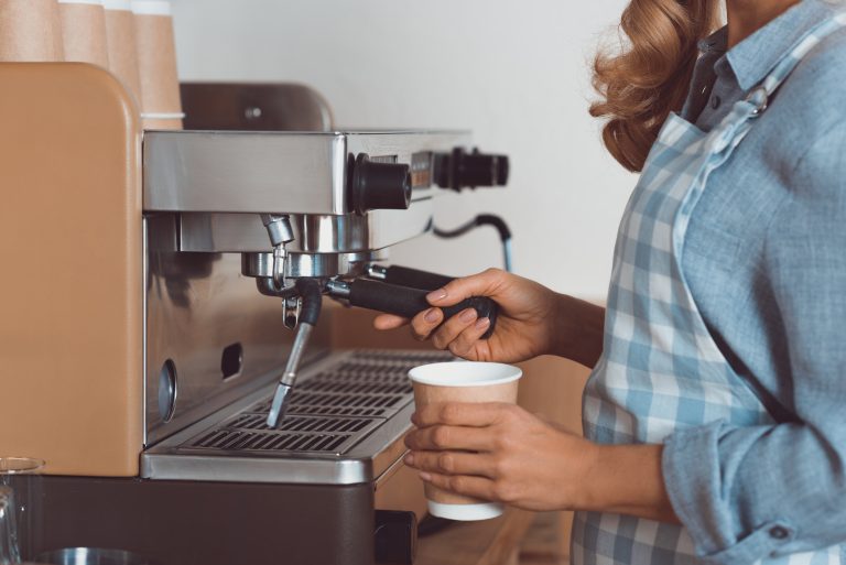 Uma mulher serve café numa máquina. A foto está cortada e não é possível ver o rosto dela