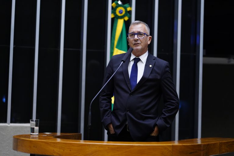 Deputado Bebeto fala ao microfone. Ele é um homem branco, grisalho e usa terno escuro e óculos