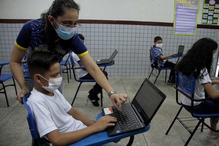 Aluno mexe num laptop com a ajuda da professora