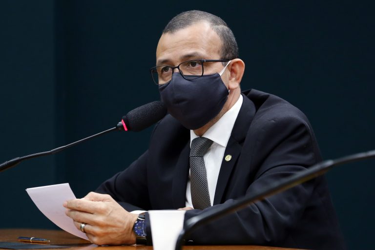 Deputado Carlos Gomes está sentado falando ao microfone