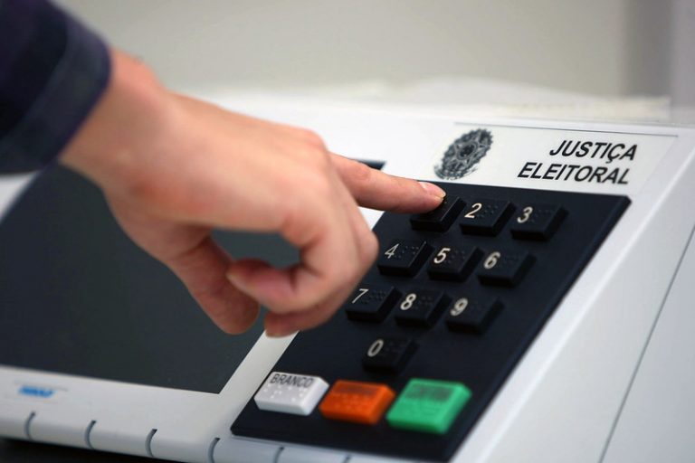 Uma pessoa vota na urna eletrônica. A foto foca na mão que aperta o número 1 na urna