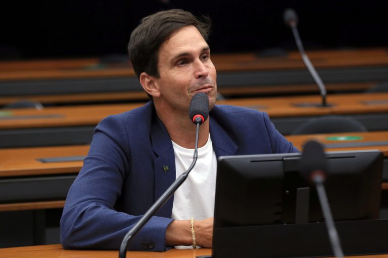 Deputado Luiz Lima está sentado falando ao microfone