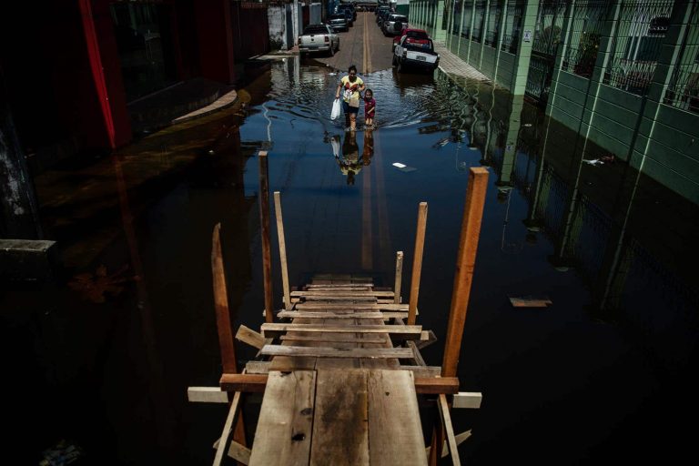 Uma mulher e uma criança caminham numa rua inundada pelas chuvas