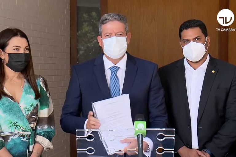 Presidente Arthur Lira segura um papel e posa para foto ao lado de dois deputados