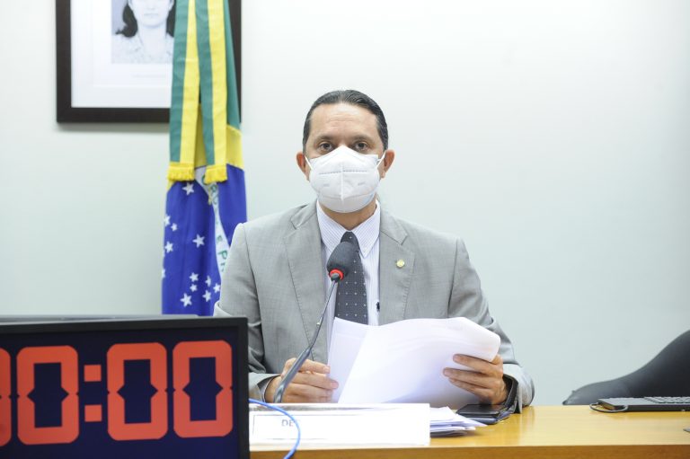 Deputado Weliton Prado usa máscara branca e está sentado com um papel nas mãos olhando para a frente