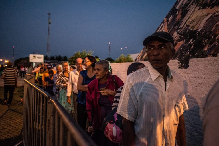 Pessoas idosas estão numa fila ao ar livre