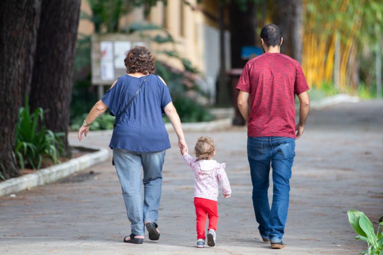Pai e mãe caminham de costas de mãos dadas com a filha pequena