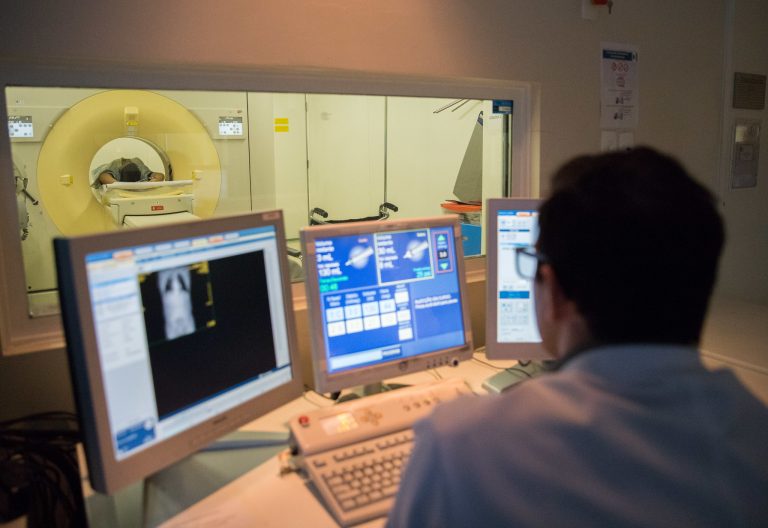 Médico analisa imagens de paciente que está numa máquina de tomografia