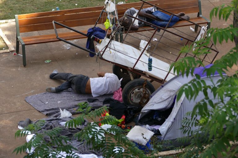 Pessoas dormem no chão e em um banco numa praça