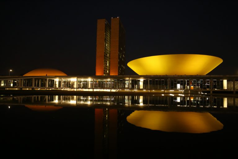 Prêdio do Congresso iluminado de laranja. Ao fundo a noite escura