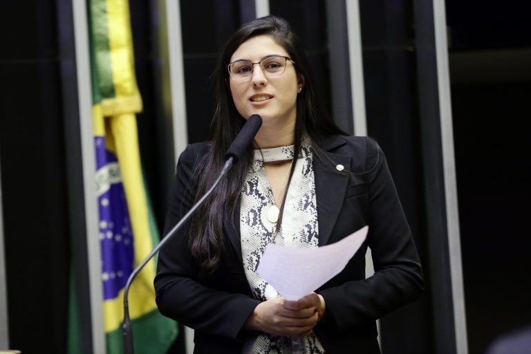 Deputada Chris Tonietto discursa no Plenário da Câmara. Ela usa blazer preto, camisa clara, tem cabelo comprido e escuro e usa óculos