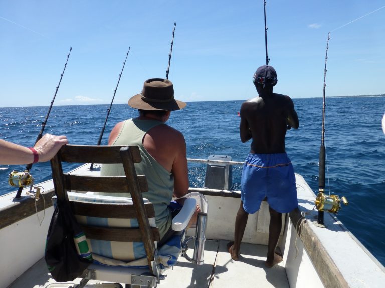 Dois homens estão num barco em alto mar pescando num dia ensolarado