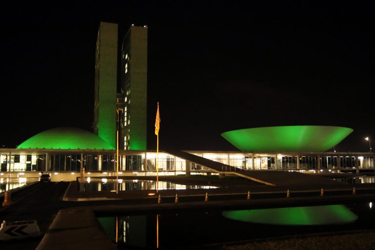 Prédio do Congresso Nacional iluminado de verde. Ao fundo a noite escura