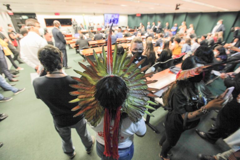 Índios reunidos num plenário usam cocares de penas