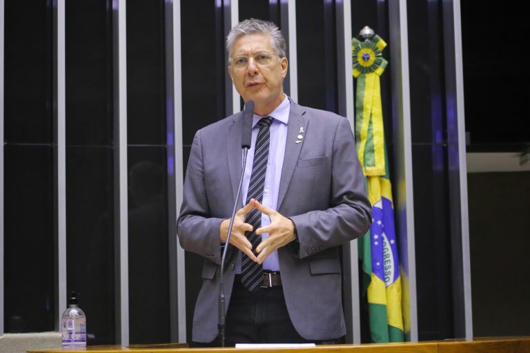 Deputado Guiga Peixoto discursa no Plenário da Câmara. Ele é branco, grisalho, usa terno cinza e óculos