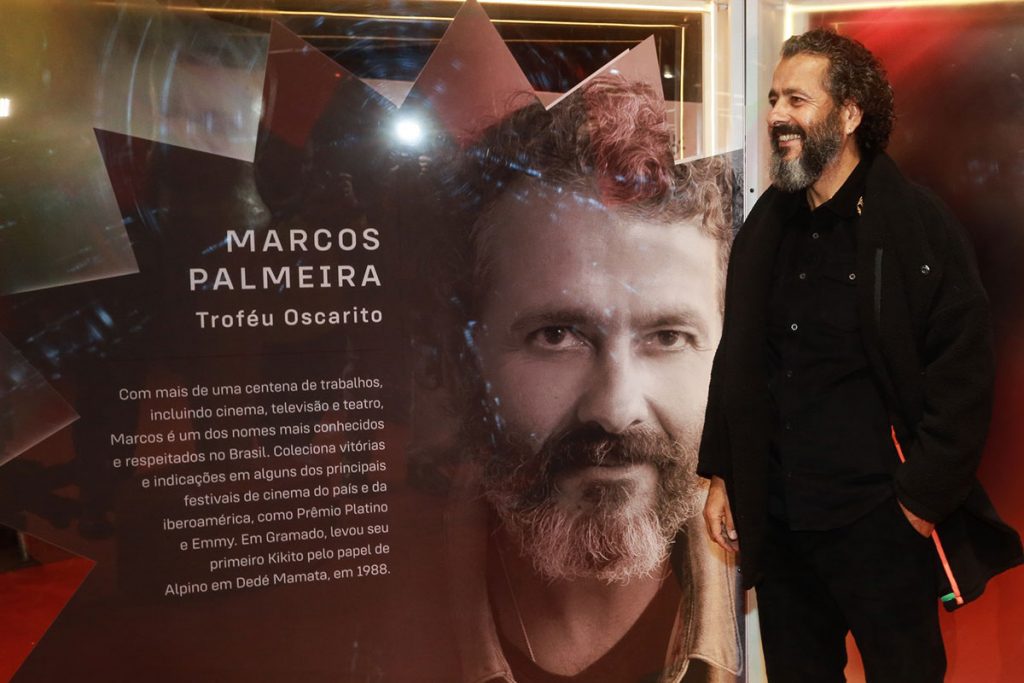 Marcos Palmeira posa ao lado da placa com texto em sua homenagem, no Festival de Cinema de Gramado