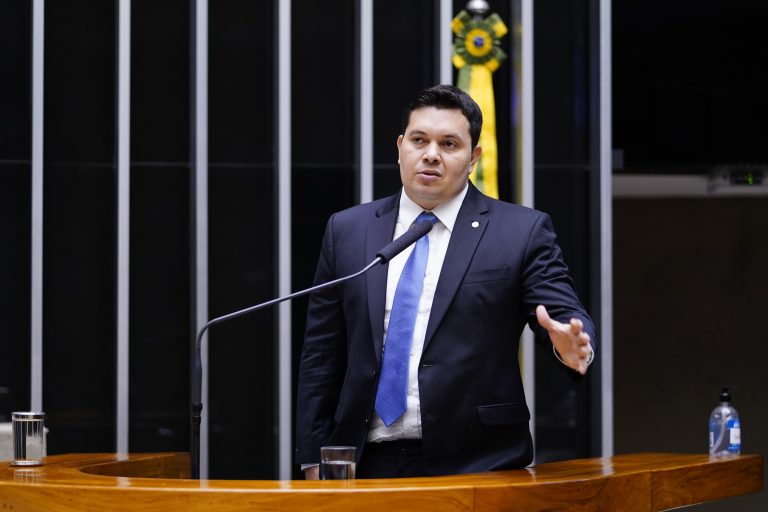 Deputado Acácio Favacho fala ao microfone. Ele é um homem branco, usa um terno escuro e camisa branca com gravata azul