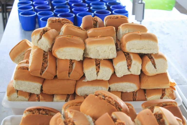Uma mesa com sanduíches empilhados e canecas azuis ao fundo