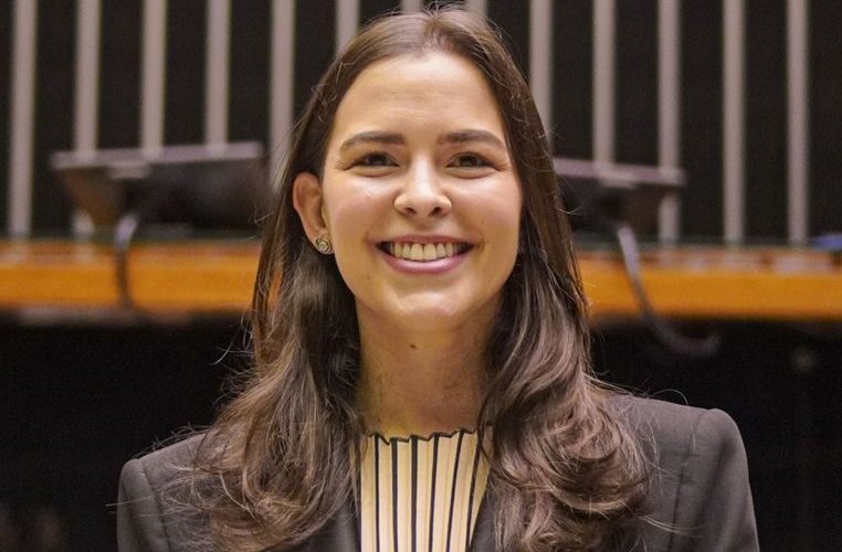 Deputada Maria Arraes sorri olhando para a câmera. Ela é uma mulher jovem, branca de cabelos longos e escuros