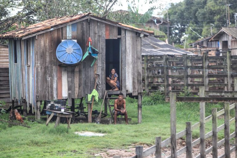Duas pessoas estão sentadas na porta de uma casa construída sobre palafitas