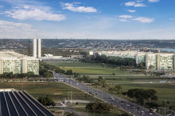 Foto aérea da Esplanada dos Ministérios em Brasília, são vários prédios altos dos dois lados e ao centro um grande gramado verde. Ao fundo está o prédio do Congresso Nacional