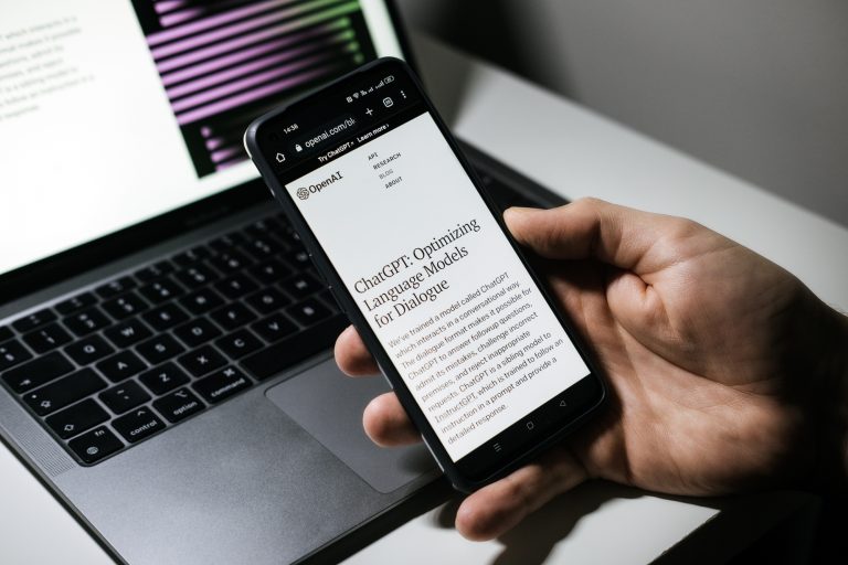 Mão segura um celular na frente de um laptop