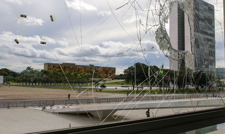 Foto de uma janela quebrada no Palácio do Planalto. Ao fundo, o prédio do Congresso Nacional